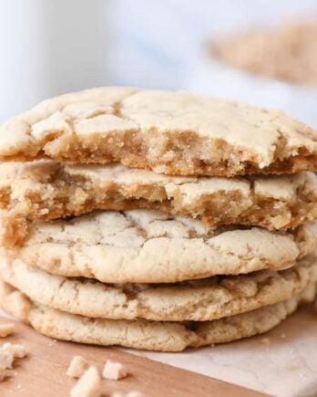 Stack of toffee cookies on wood cutting board with one cookie broken in half.