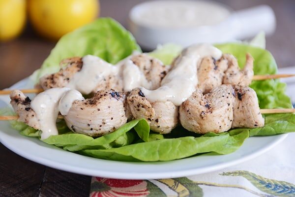 Grilled chicken skewers laying on lettuce leaves and drizzled with sauce.
