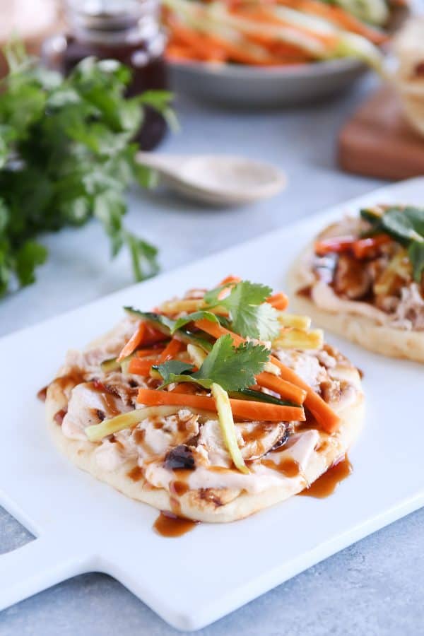 Chicken banh mi flatbread with pickled cucumbers and carrots on white platter.