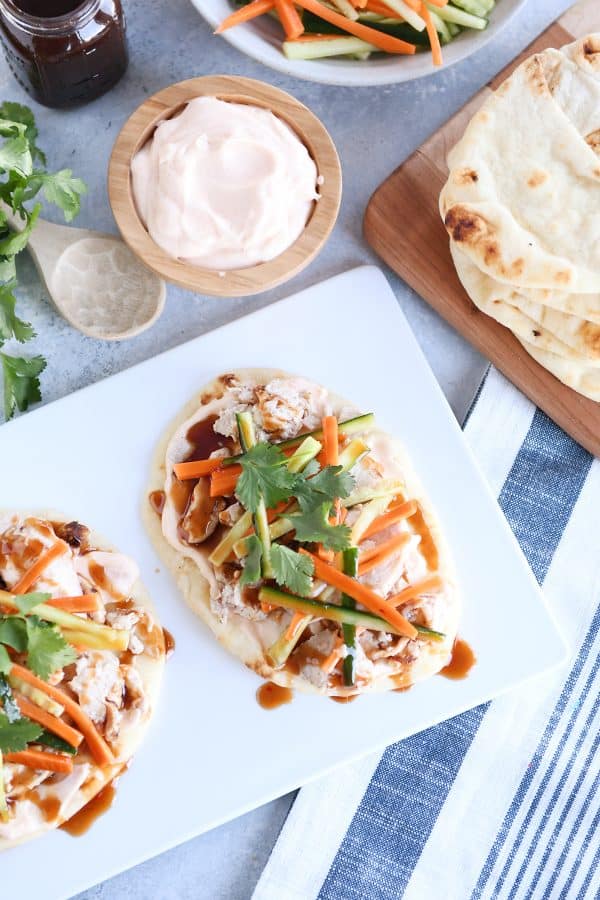 Top down view of Chicken banh mi flatbread with pickled cucumbers and carrots on white platter.