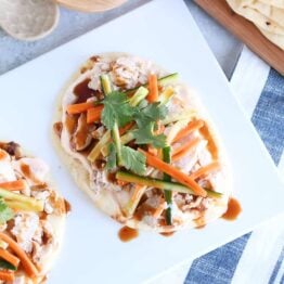 Top down view of Chicken banh mi flatbread with pickled cucumbers and carrots on white platter.