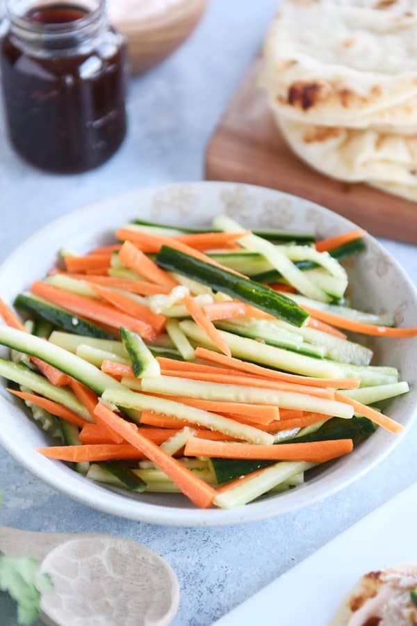 Tan bowl filled with pickled cucumber and carrot sticks.