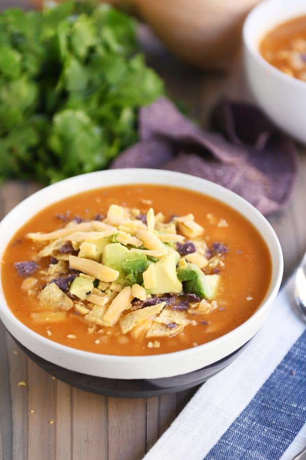 Chicken enchilada soup in tan bowl with brown stripe.