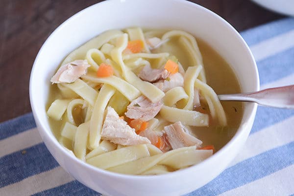 A white bowl of chicken noodle soup with a spoon in the side.