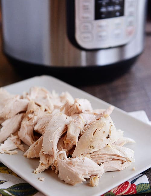 Cooked, shredded chicken on a white plate, in front of an Instant Pot.