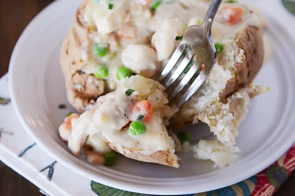 A baked potato with chicken pot pie sauce on top and a fork taking a bite out.