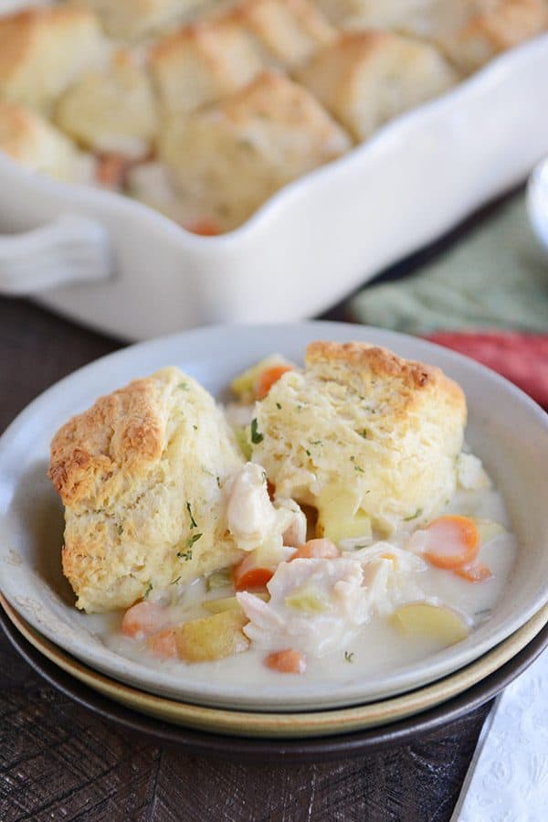 a white bowl with chicken pot pie filling and two cooked biscuits on top