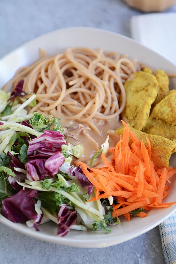 A white bowl of salad, shredded carrots, chicken, noodles, and dressing in the middle.