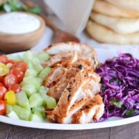 White platter with grilled chicken shawarma, cucumbers, tomatoes and cabbage slaw.