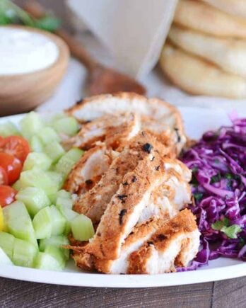 White platter with grilled chicken shawarma, cucumbers, tomatoes and cabbage slaw.