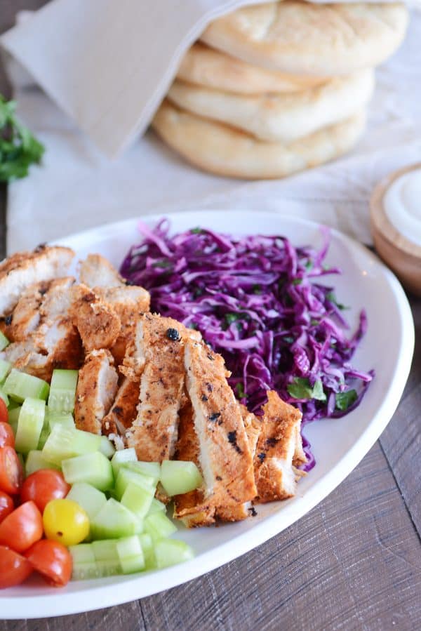 White platter with grilled chicken shawarma, cucumbers, tomatoes and cabbage slaw.