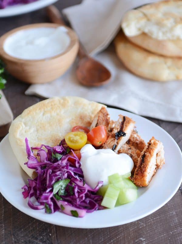 White plate with slices of chicken shawarma, yogurt sauce, flatbread and vegetables. 