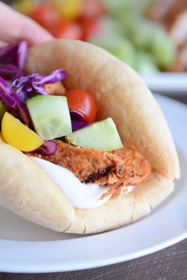 Pieces of grilled chicken shawarma with yogurt sauce and vegetables in flatbread.