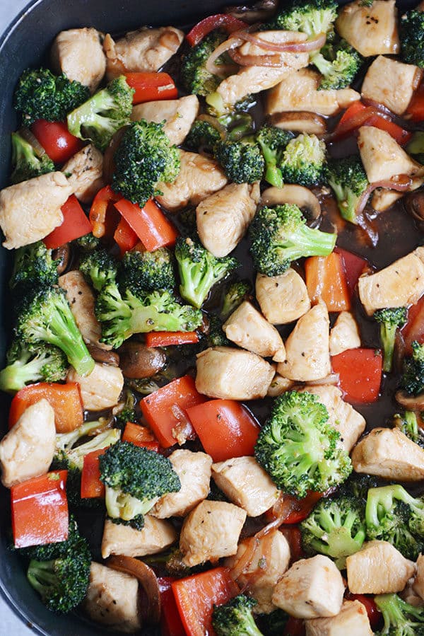 Top view of a skillet of cooked chicken, broccoli, peppers, and onions.