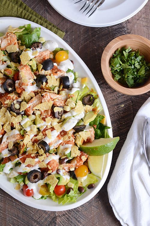 A white oval bowl full of a chicken taco salad drizzled with dressing.