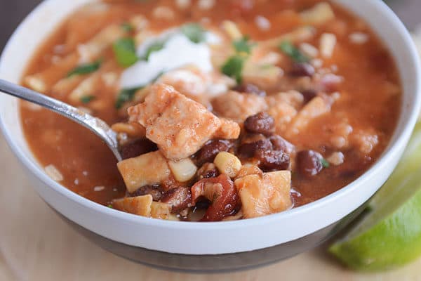 A spoon taking a bite out of a bowl of red chicken tortilla soup. 