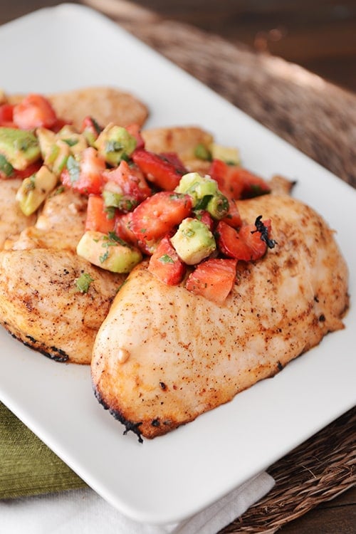 A white tray of grilled chicken breasts topped with strawberry-avocado salsa.