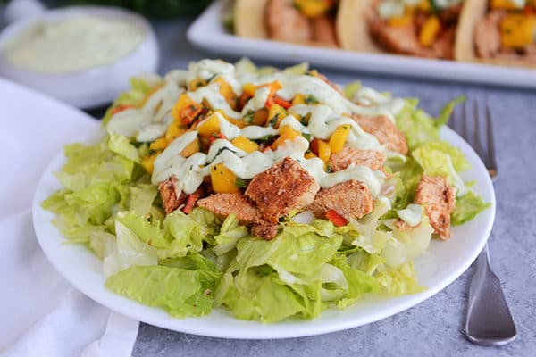 A green salad topped with chicken and vegetables on a white plate.