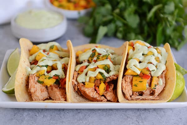 Three chili lime pork tacos in corn tortillas lined up on a white platter.