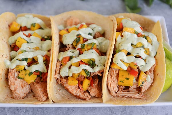 Top view of pork and veggie tacos on a white platter drizzled with a green dressing.