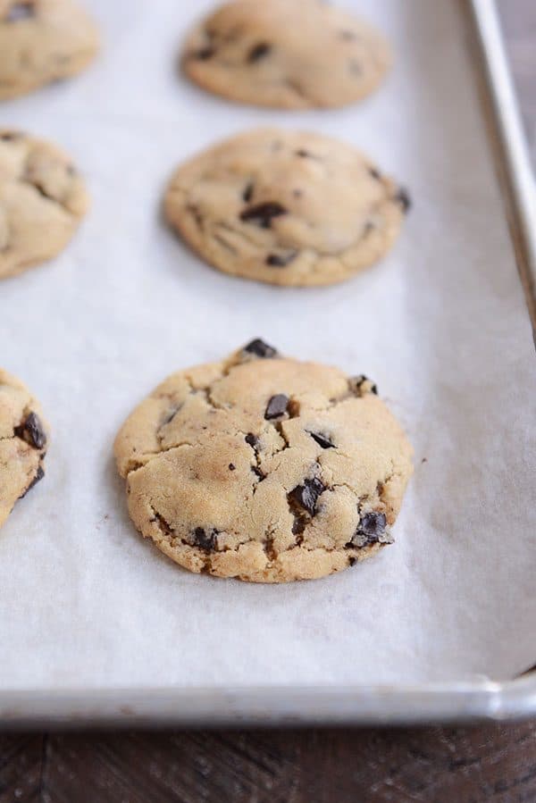 Baked chocolate chip cookies on a parchment-lined cookie sheet.