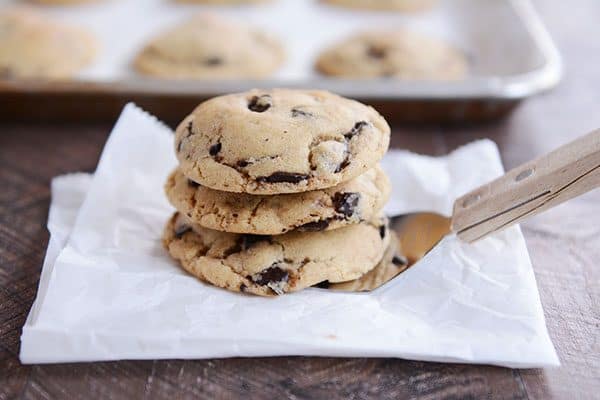 Three chocolate chip cookies stacked on a metal spatula.