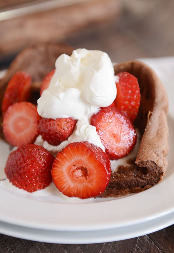 A square of chocolate dutch baby pancake topped with whipped cream and sliced strawberries.