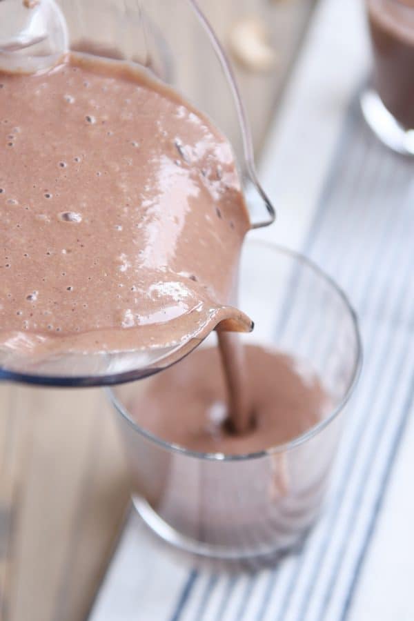 Pouring chocolate protein smoothie into glass.