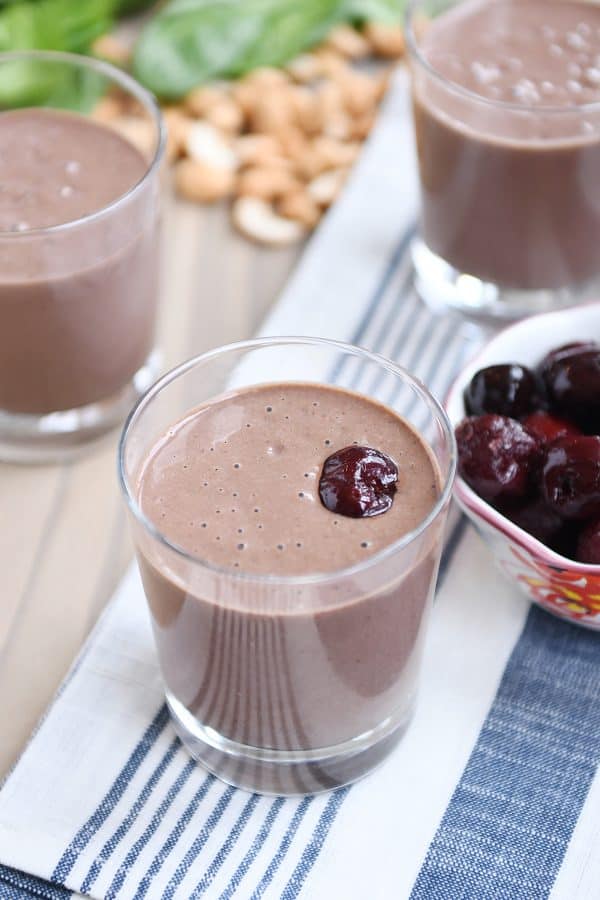 Chocolate protein smoothie in clear glass with cherry on top.