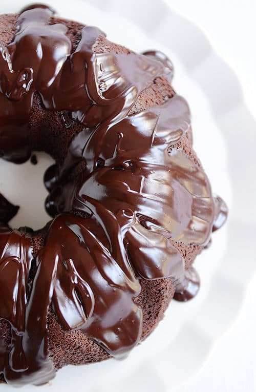 Top view of a ganache covered chocolate bundt cake on a white cake platter.