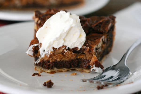 A slice of chocolate caramel pecan pie with a bite taken out.