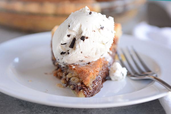 A slice of chocolate chip cookie pie with a scoop of vanilla ice cream on the top.