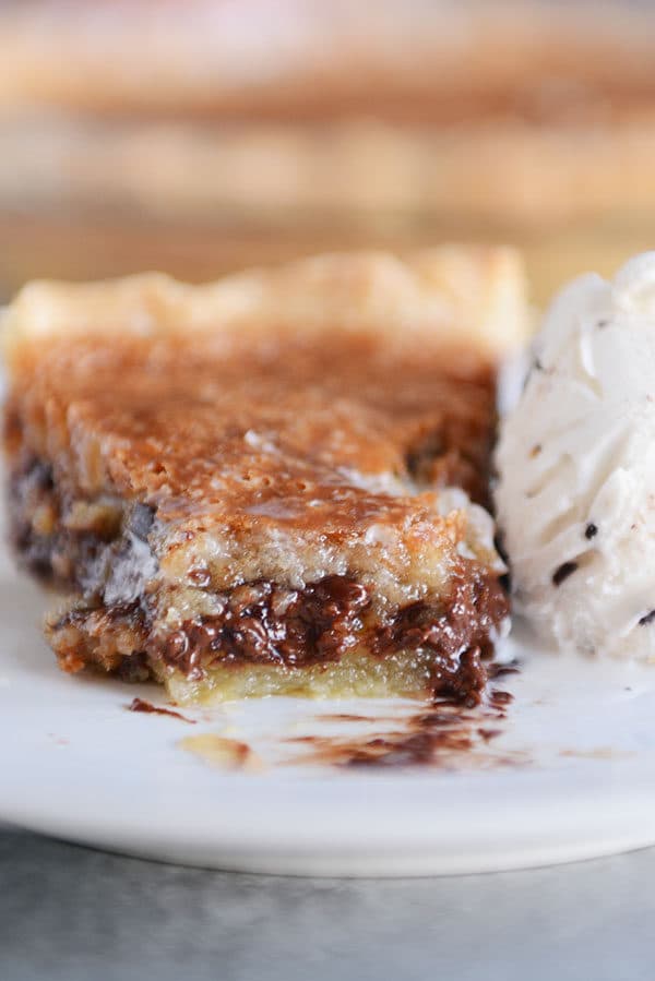 A slice of gooey chocolate chip pie with a bite taken out on a white plate.