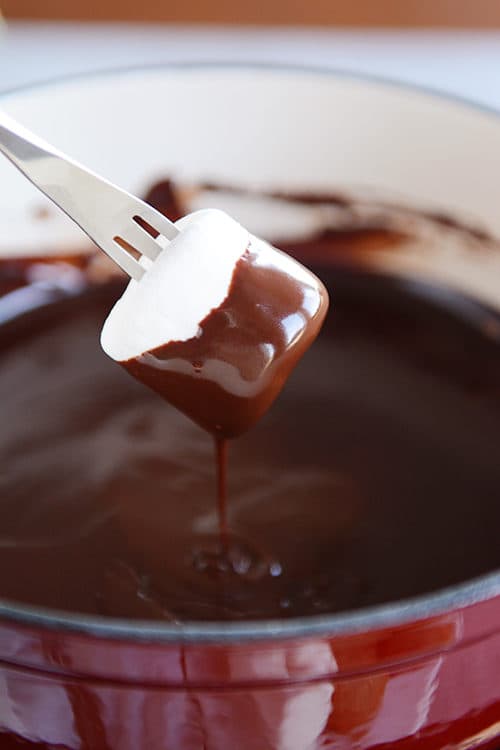 A half dipped marshmallow over a a pot of chocolate fondue.