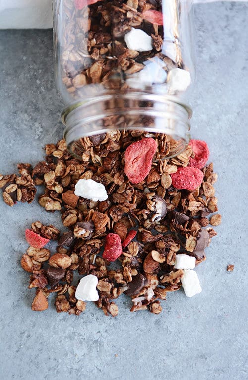 Dark chocolate and strawberry granola spilling out of a glass mason jar.