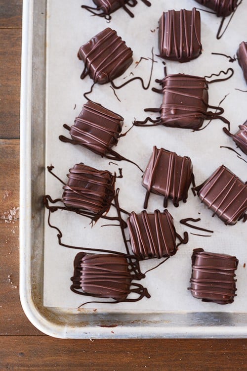 A cookie sheet full of chocolate dipped and drizzled caramels.