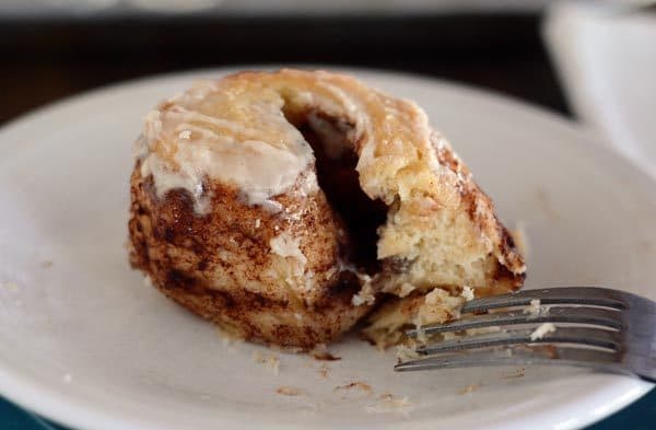 The middle part of a cinnamon roll on a white plate, with a fork on the side.