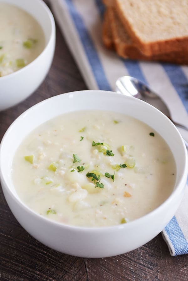A white bowl of New England clam chowder with parsley sprinkled on top.
