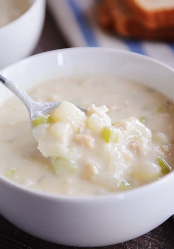A spoon taking a big bite of clam chowder out of a white bowl.
