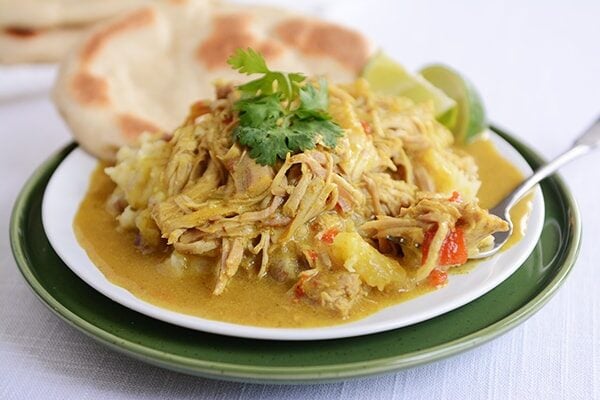 A white plate of shredded pork curry with flatbread on the side.