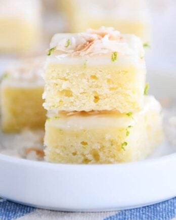 Toasted coconut lime bars stacked on white circle plate.