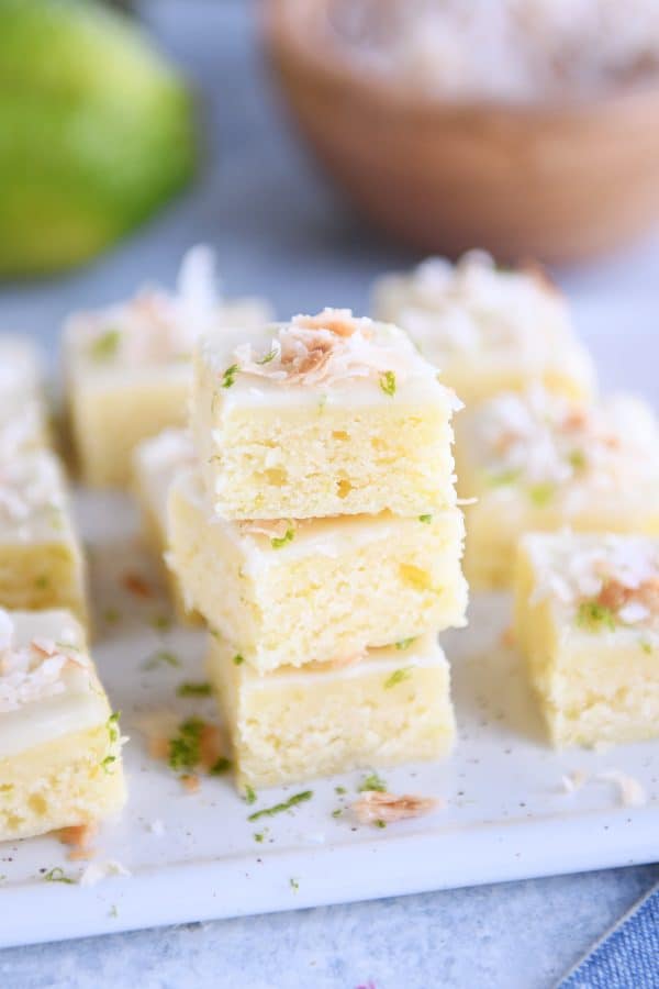 Toasted coconut lime bars stacked on white platter.