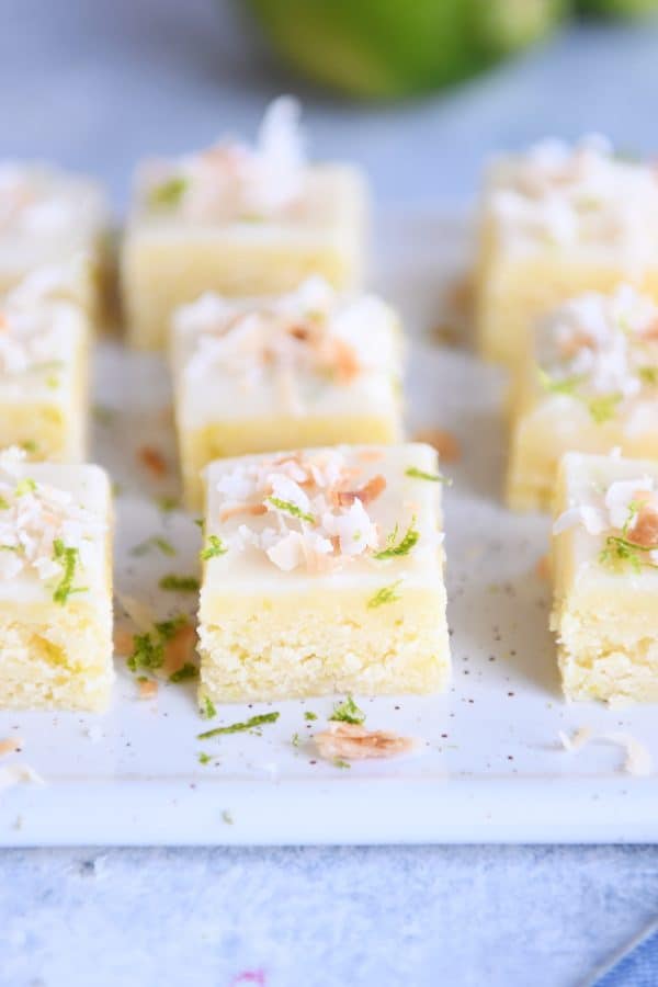 Toasted coconut lime bars cut into little squares on white platter.