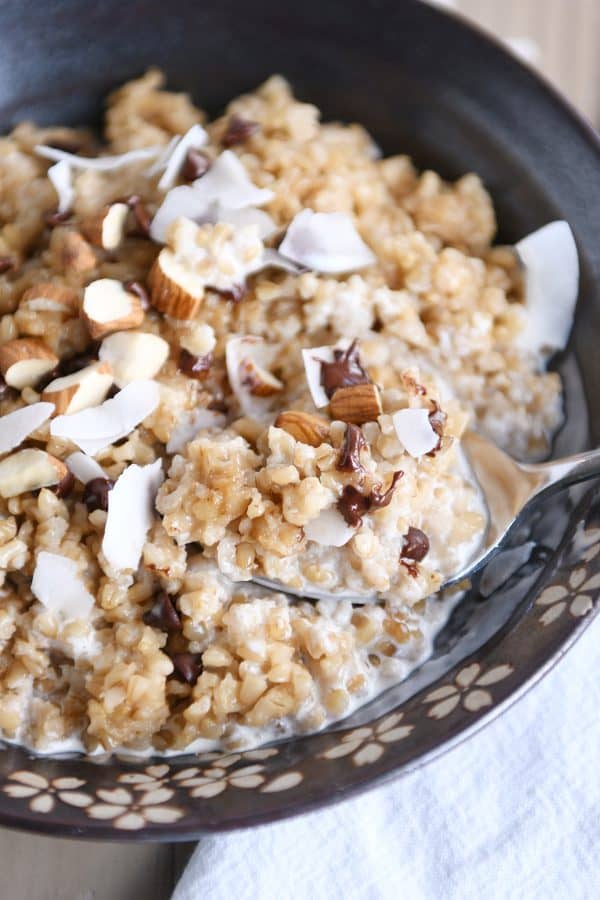 Coconut milk steel cut oats in brown bowl with chocolate chips, almonds and coconut.