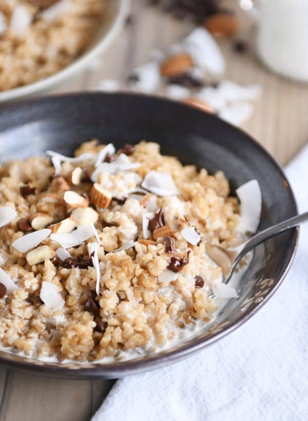 Coconut milk steel cut oats in brown bowl with chocolate chips, almonds and coconut.