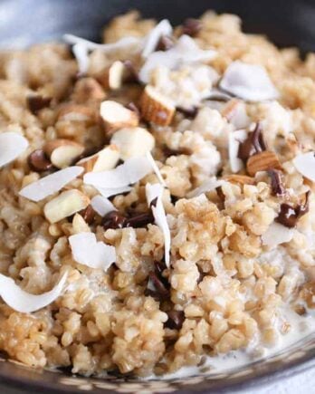 Coconut milk steel cut oats in brown bowl with chocolate chips, almonds and coconut.