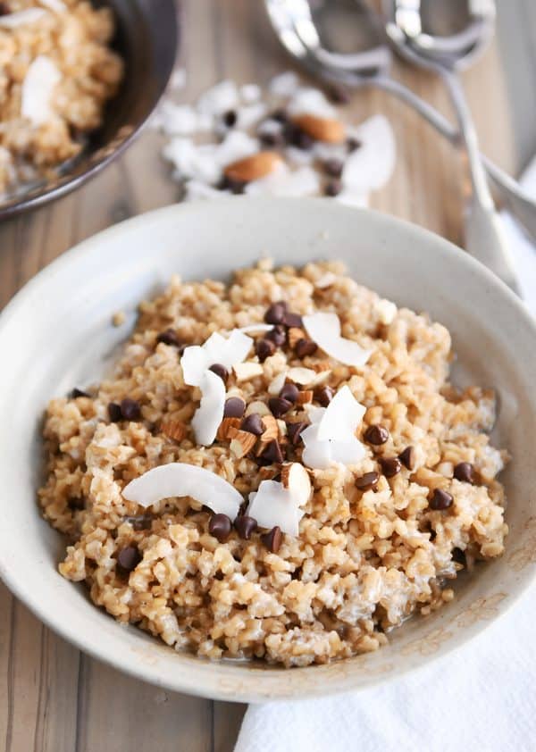 Coconut milk steel cut oats in white bowl with chocolate chips, almonds and coconut.