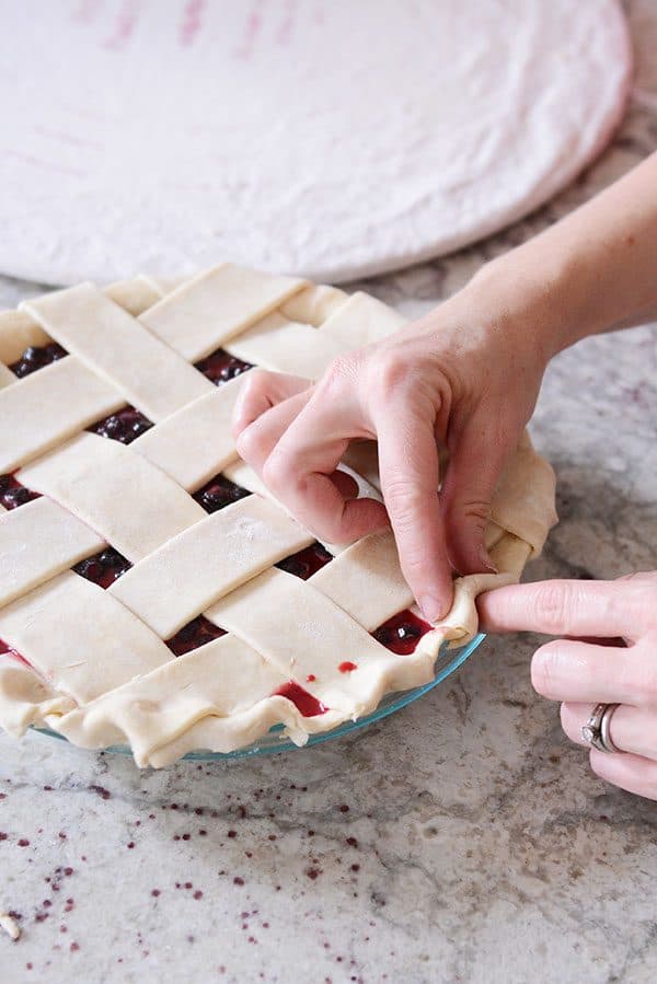 An uncooked lattice pie crust getting the sides crimped.