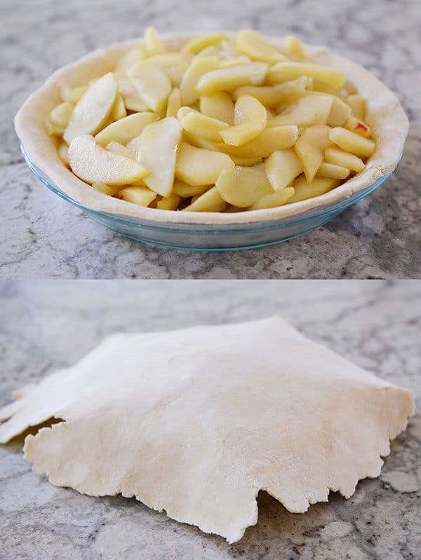 A pie full of apples and an uncooked crust getting laid over the top.