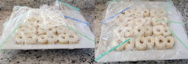 two trays of frosted sugar cookies covered with straws and saran wrap to protect the frosting.